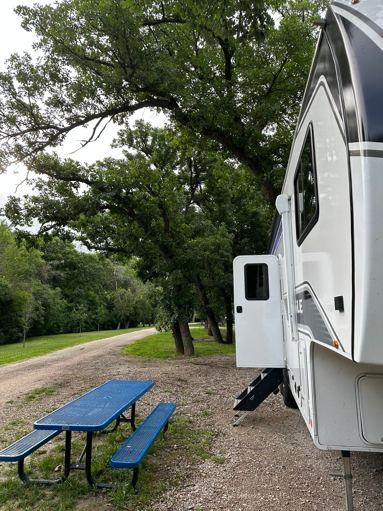Fifth wheel at a shaded campsite with a blue picnic table at Ravenna Lake, Buffalo County Recreation Area