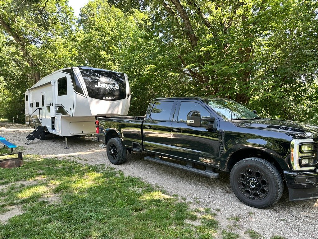 Jayco fifth wheel and F-350 parked at a gravel pull-through site under the trees at Ravenna Lake, Nebraska